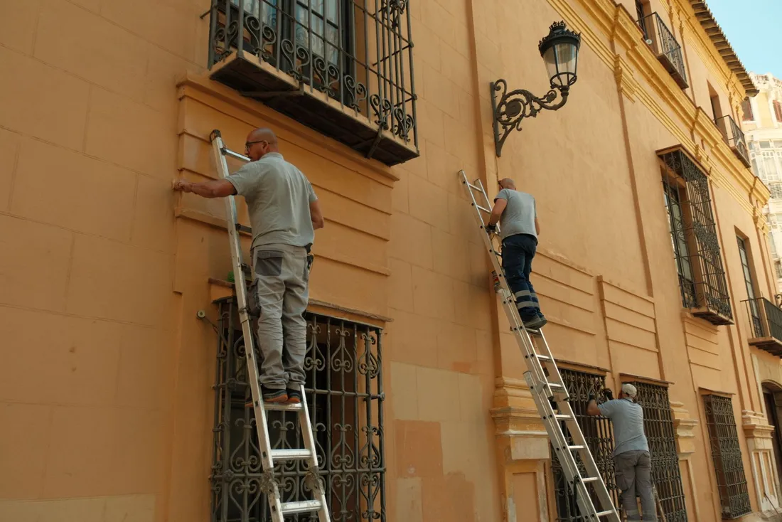 Ouvriers sur des échelles reprenant la façade enduite d'un immeuble ancien à balcons en fer forgé (Senouillac, Tarn)