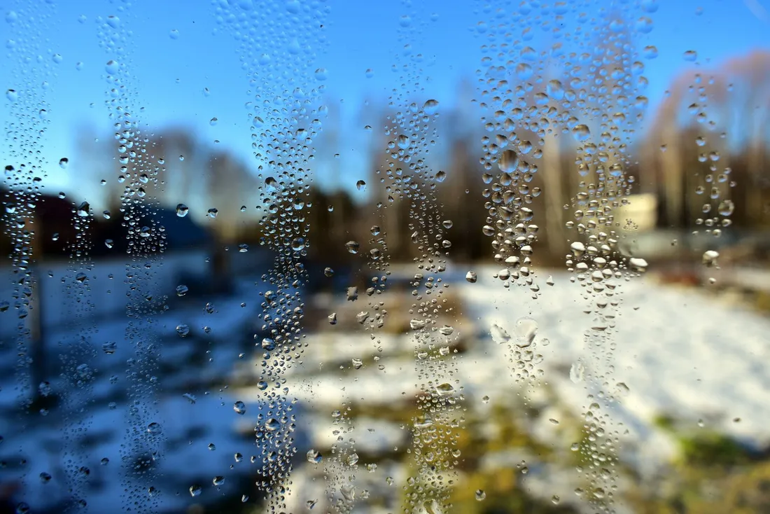 Gouttes de condensation ruisselant sur une vitre, jardin enneigé à l'extérieur