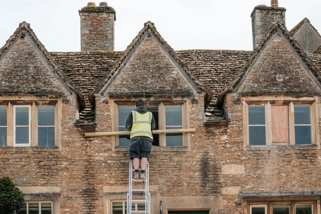 Ouvrier sur une échelle réparant une fenêtre dans une façade en pierre blonde à pignons (Roanne, Loire)