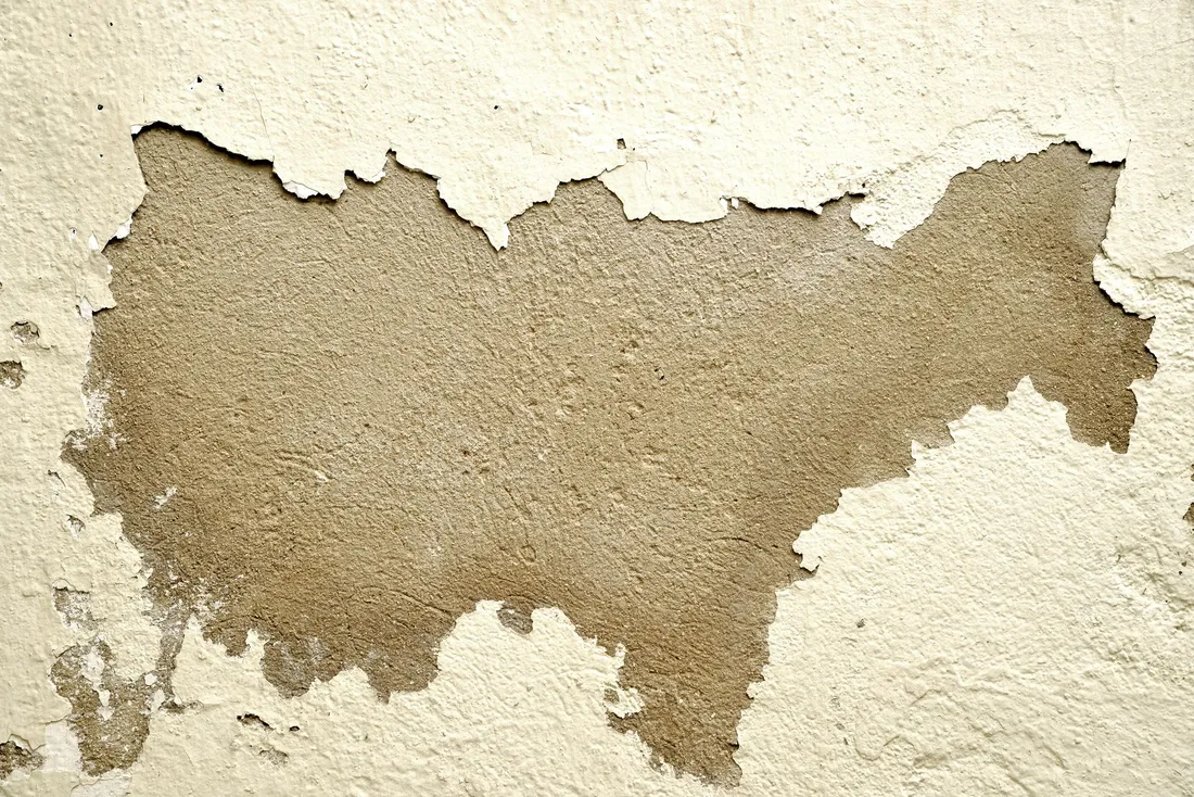Plaque de peinture crème arrachée sur un mur, laissant apparaître l'enduit brun et rugueux