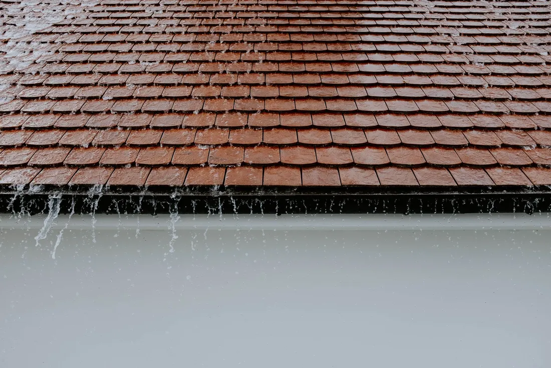 Averse sur une toiture de tuiles brunes, l'eau goutte en rideau au bord du toit (Lezoux, Puy-de-Dôme)