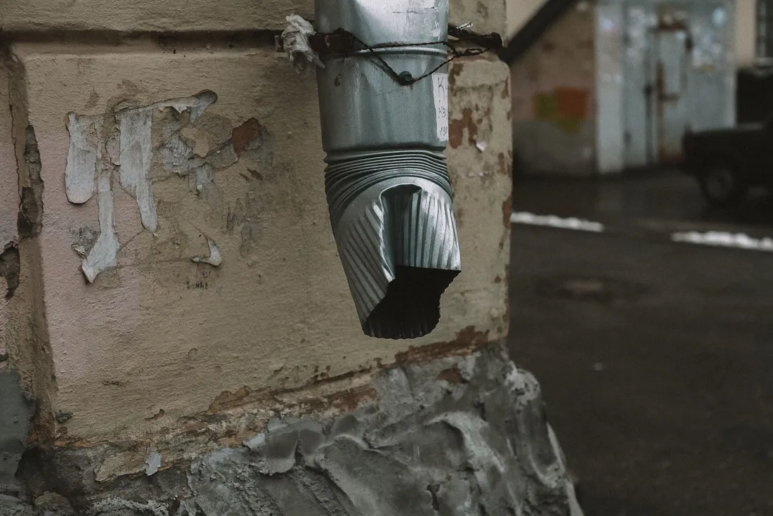 Descente d'eau pluviale cabossée contre un mur dont la peinture s'écaille en plaques (Sain-Bel, Rhône)