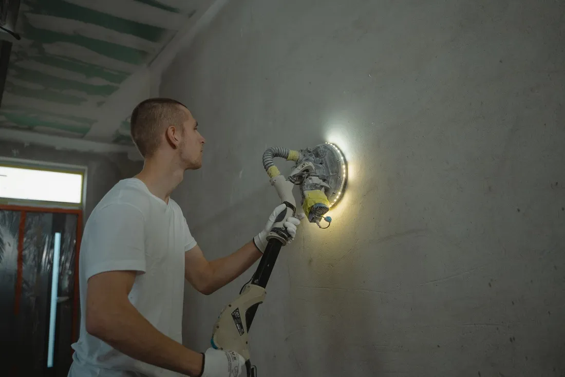 Ponçage d'un mur intérieur à la ponceuse à bras avant la mise en peinture