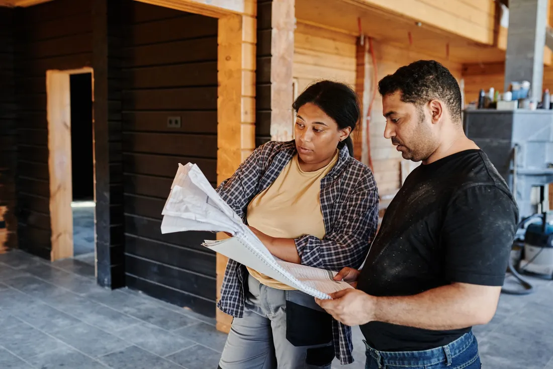 Deux personnes relisant des plans papier dans une maison en travaux
