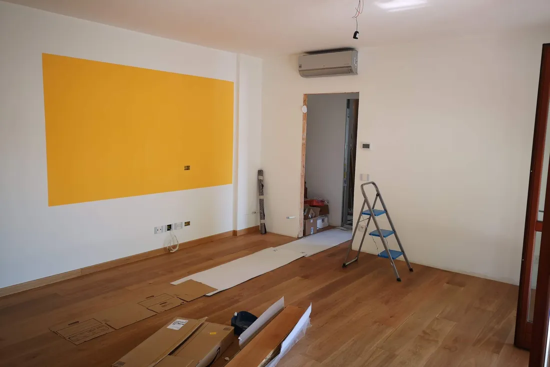 Pièce vide en fin de chantier : parquet neuf, escabeau et pan de mur peint en jaune
